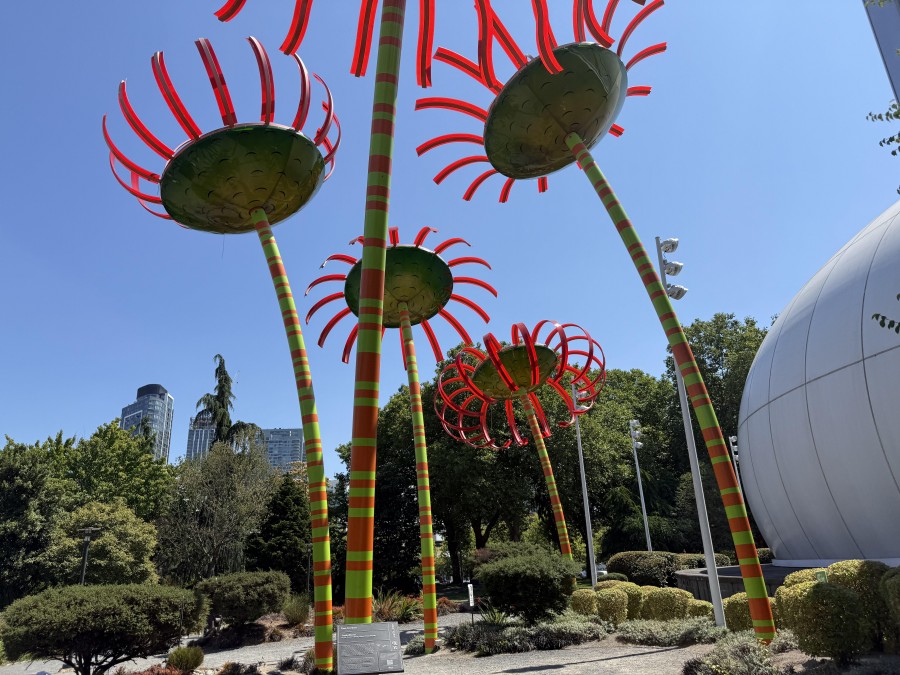 The renovated Space Needle stands tall beside the whimsical “Sonic Bloom” flower sculptures—towering, brightly colored art installations that resemble futuristic blossoms.