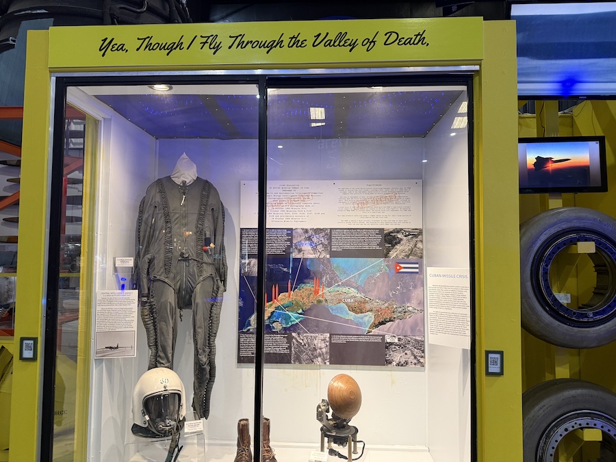 A glass display case featuring a vintage flight suit, helmet, and boots.