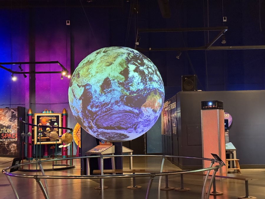 A large illuminated globe displaying Earth in a darkened exhibit hall.