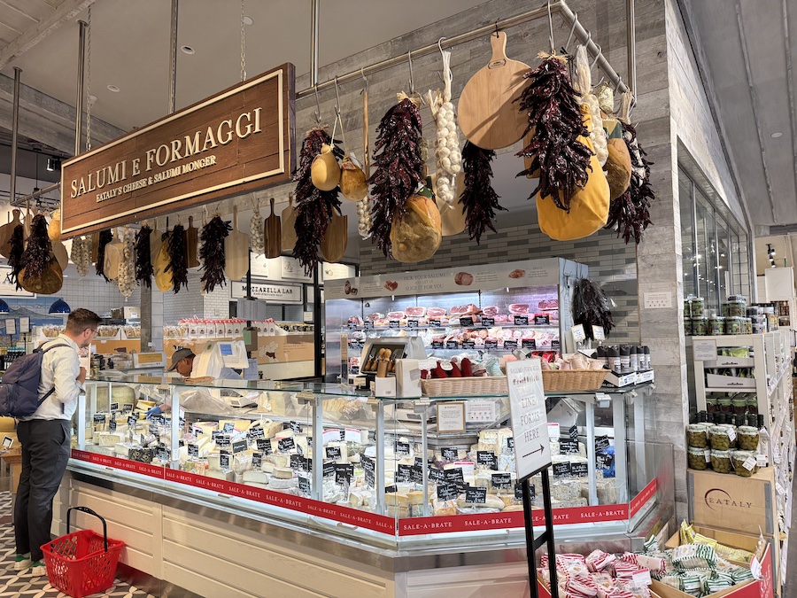 A deli counter at Eataly showcasing hanging salami and fresh cheeses.