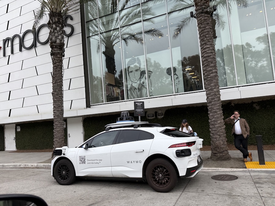 Self-driving Waymo car with white exterior and Waymo logo on the side.