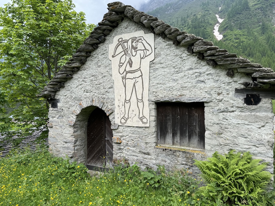 A small, rustic stone building stands on a grassy hill.