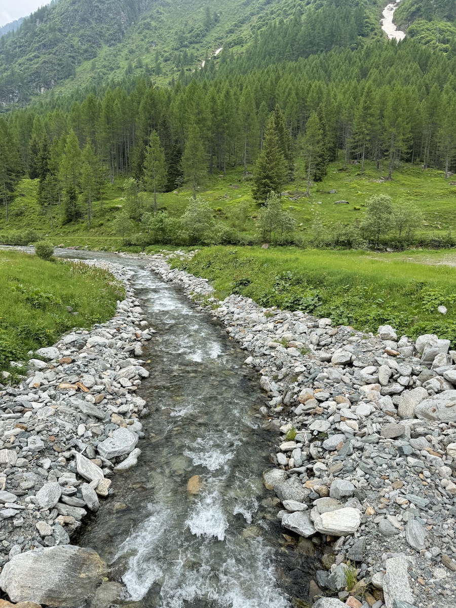 A clear, rocky stream flows through a lush, green valley. 