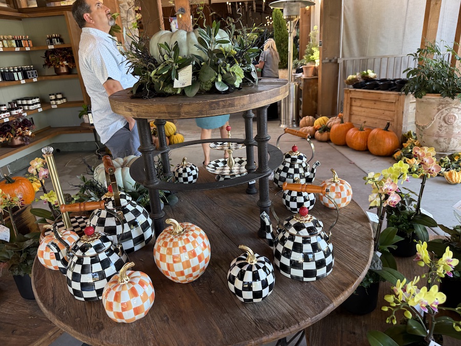 A round wooden table displays an array of decorative teapots and pumpkins in checkered patterns.