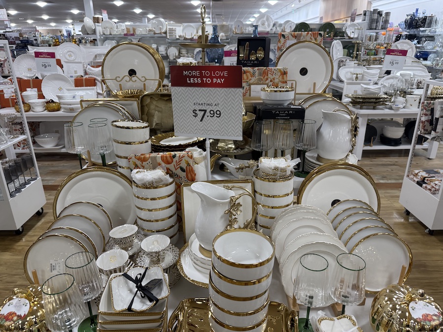 A prominent display table showcases a collection of elegant white dinnerware with a gold-rimmed design.