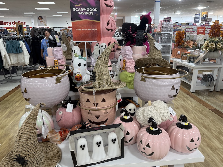 A large display table features an assortment of whimsical Halloween decor, primarily in pink and black.
