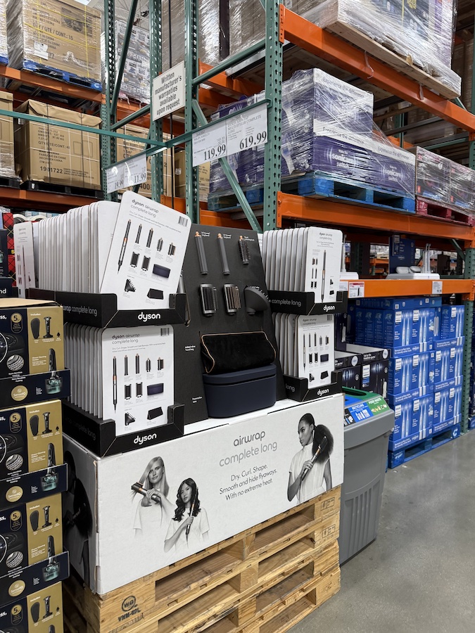 Shelves at Costco displaying boxed Dyson Airwrap Multi-Styler Complete Long hair tools with promotional tags and product information.