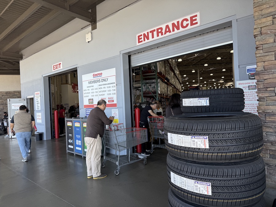 The main entrance of a Costco warehouse with shopping carts, and posted member open hours visible on the wall.