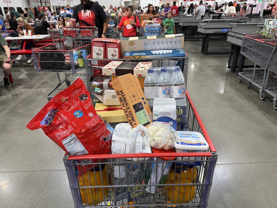 Full Costco shopping cart packed with bulk snacks, desserts, and festive products.