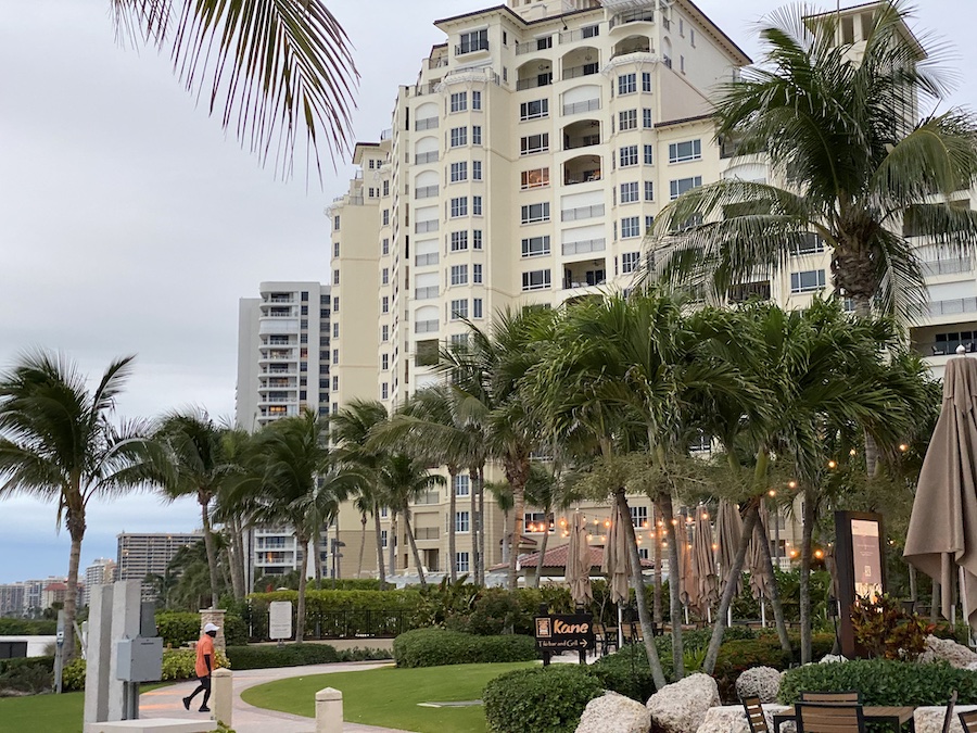 A view of the resort grounds featuring a paved walkway, vibrant green lawn, and numerous tall palm trees.