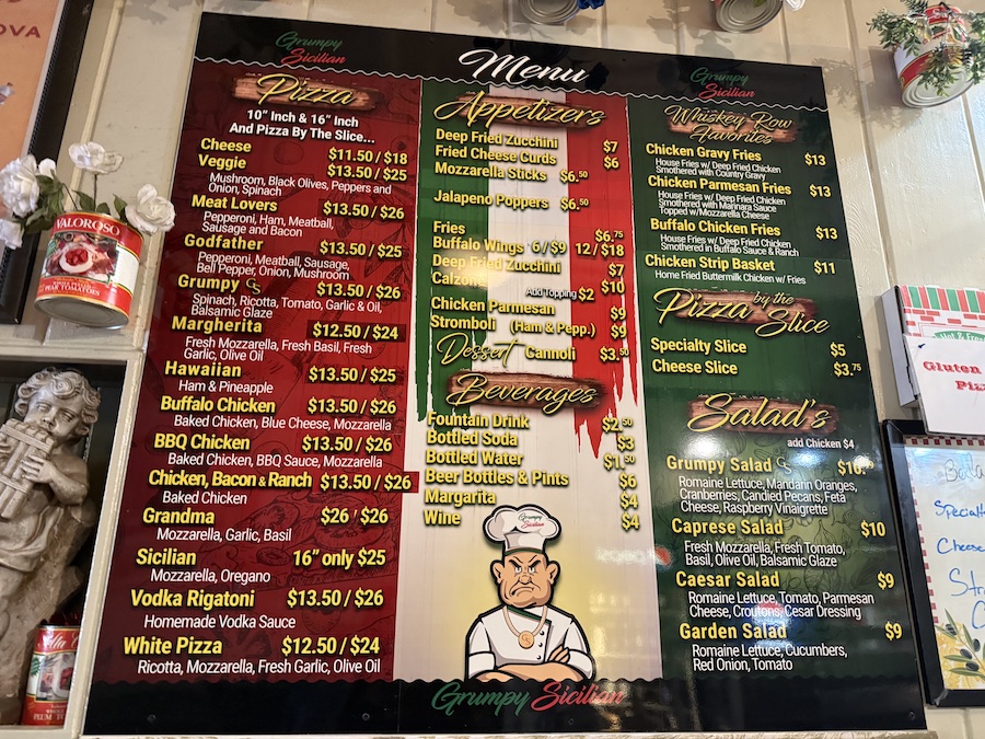 Grumpy Sicilian menu with bold fonts and creative pizza names displayed on a rustic wooden counter.