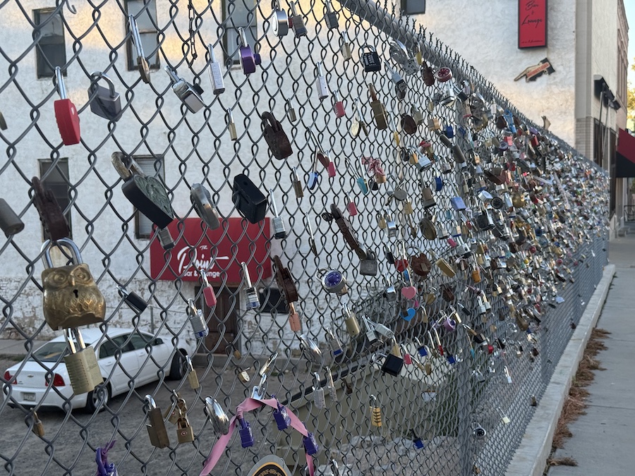 A metal fence covered with colorful love locks near a scenic Prescott overlook, symbolizing friendship and romance.