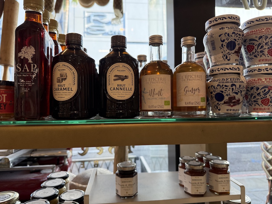 Close-up of glass bottles of artisanal syrup beside jars of preserves.