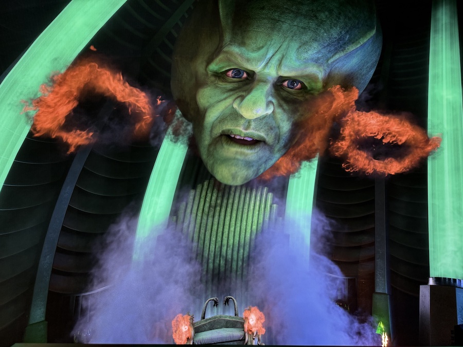 A dramatic, highly detailed close-up shot of the massive, frightening face of the Wizard of Oz as he appears on the giant screen.