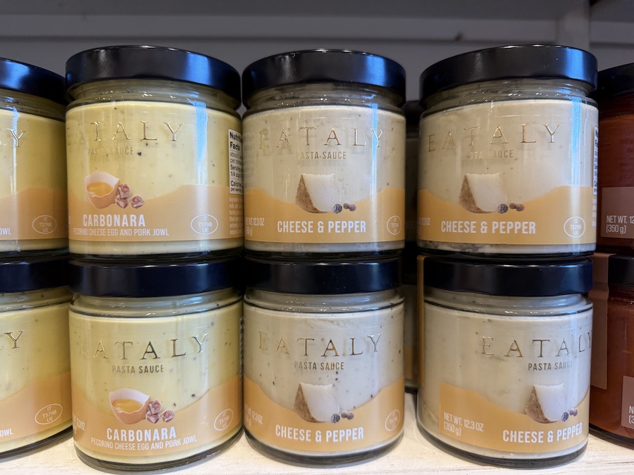 Signature Eataly-branded pasta sauces in jars with minimalist Italian labels, arranged in neat rows.