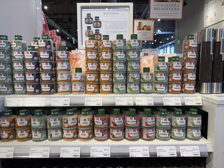 Shelves lined with colorful Montosco jars of Italian herbs and spices, beautifully arranged in the Eataly LA market section.
