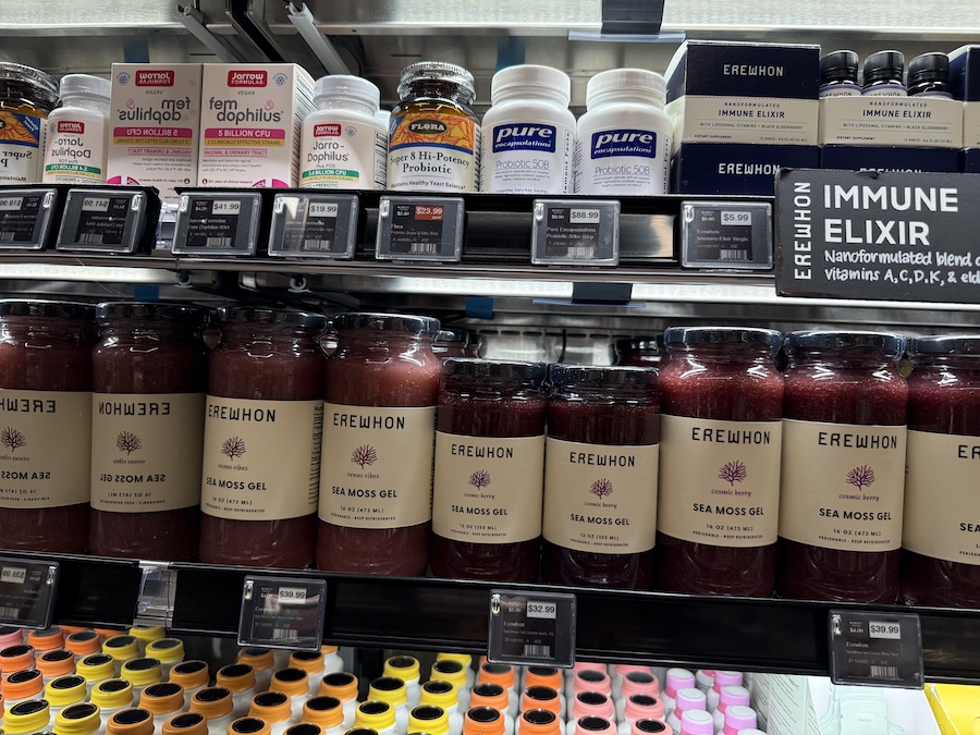 Jars of Erewhon Sea Moss Gel in various natural flavors, arranged in a refrigerated case promoting gut and skin health.