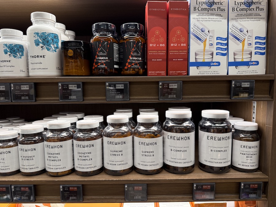 Close-up of vitamin bottles from LivOn, Cymbiotica, Dr. Nigma, Thorne, and Erewhon neatly arranged on a wooden health aisle shelf.