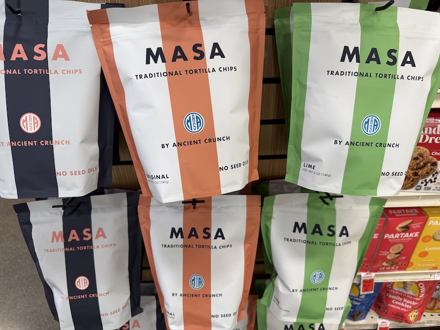 Artisan-style MASA tortilla chips arranged in rustic packaging on store shelves.