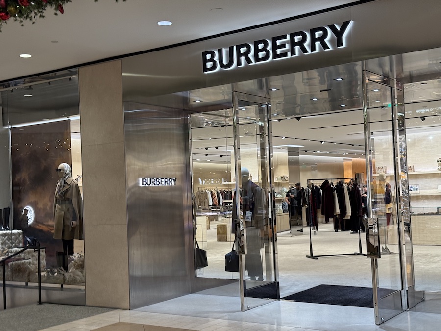 The Burberry store with modern displays of trench coats and handbags, and warm holiday-themed lighting.