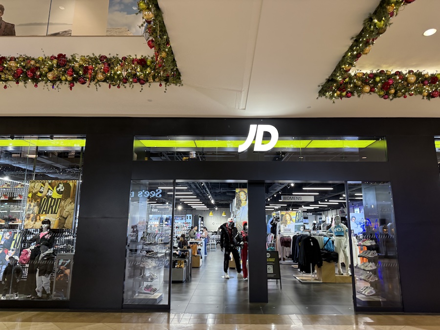 The JD Sports store with racks of sneakers and athletic wear, sleek black signage, and illuminated brand logos inside a modern retail space.