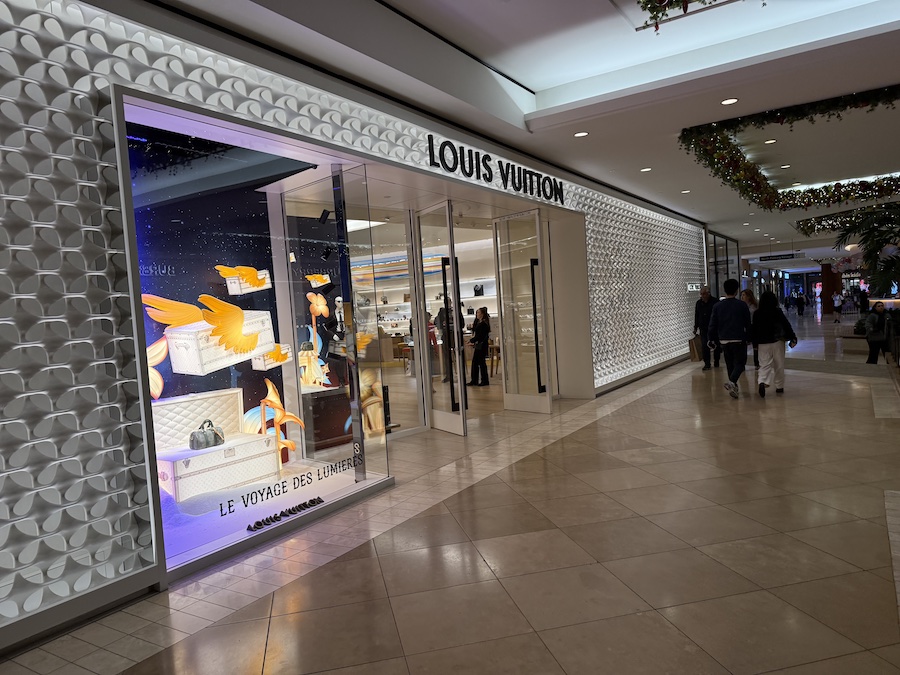 The Louis Vuitton boutique showcasing the signature LV monogram pieces, bright interior lighting, and a large illuminated logo on the wall.