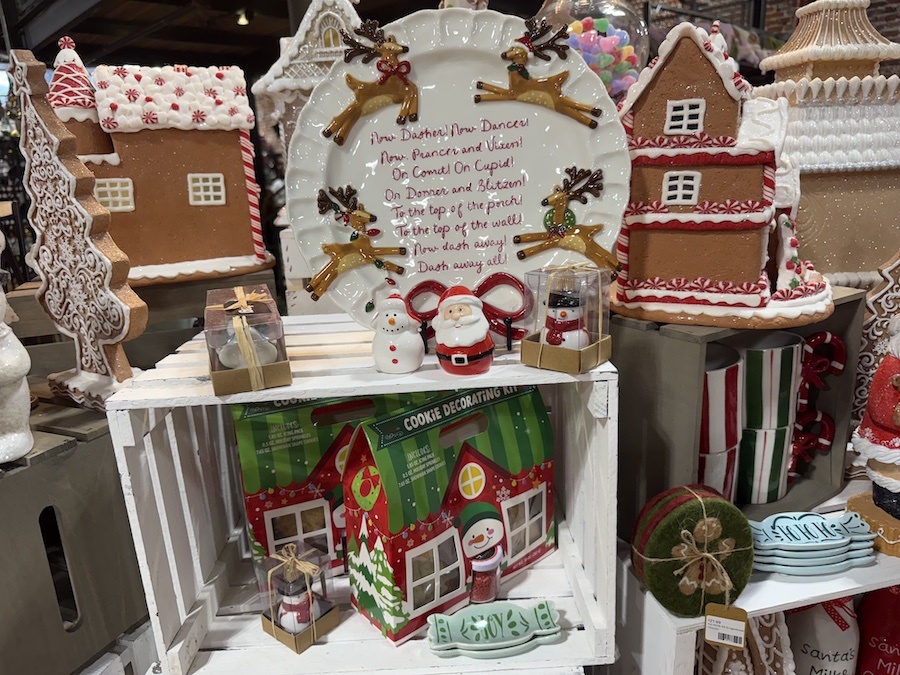 A tall shelf filled with Christmas kitchen décor—spice jars with holiday labels, Christmas-tree-shaped salt and pepper shakers, festive kitchen timers, and red-and-white utensils.