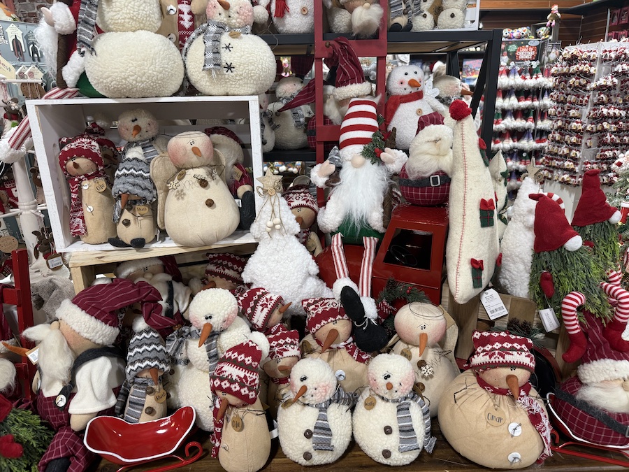 Soft plush snowmen with cozy scarves and hats, grouped on a festive shelf.