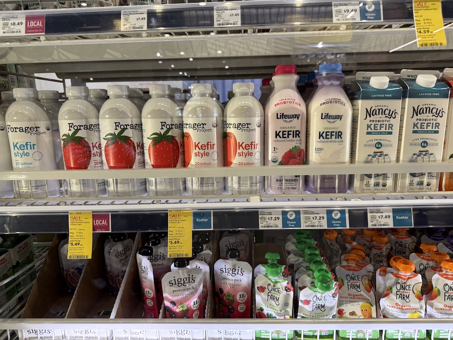 Assortment of probiotic kefir bottles from Forager, Lifeway, and Nancy’s on a chilled grocery shelf.