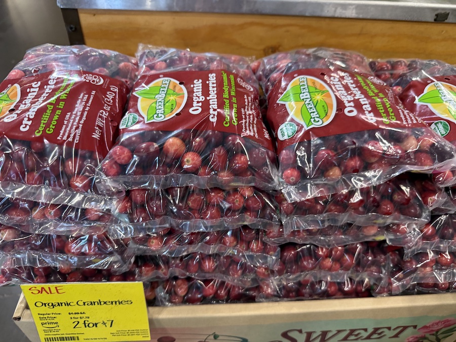 Bins of fresh organic cranberries in the produce section, glistening under bright market lighting.
