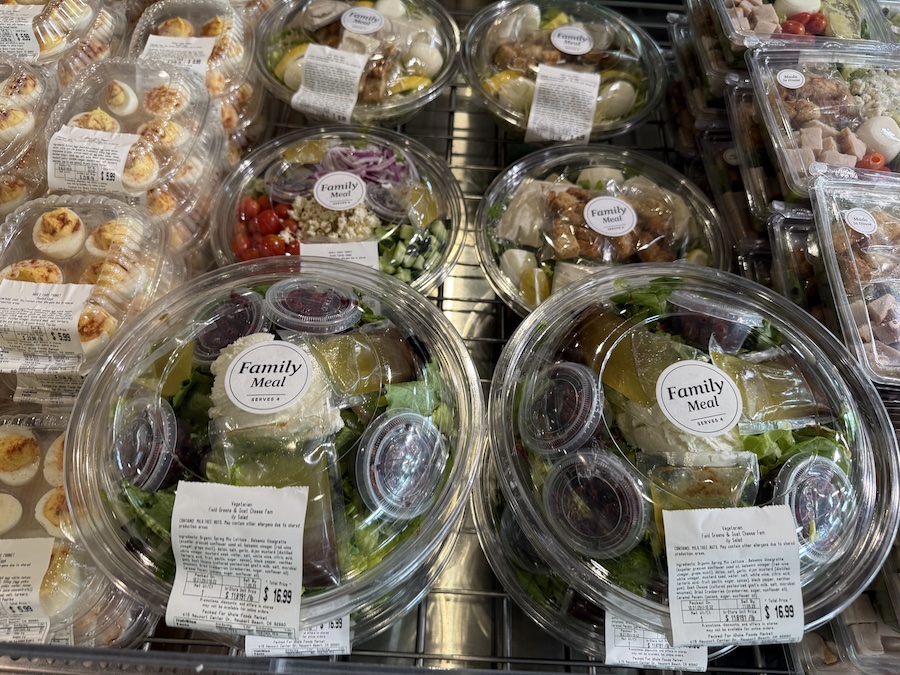 A vibrant salad bar featuring pre-packed leafy green salads in clear containers.