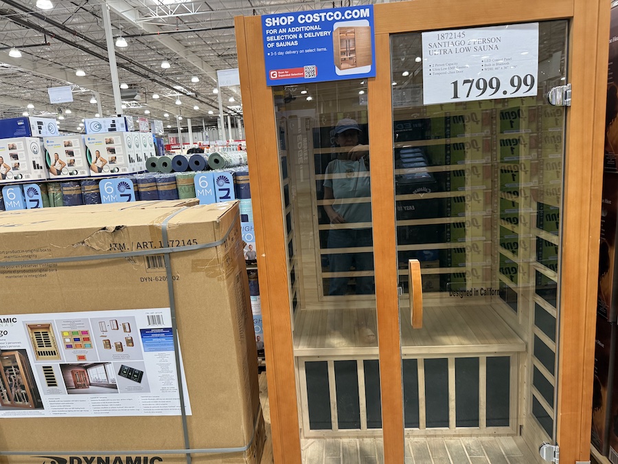 A wooden two-person infrared sauna stands assembled in the warehouse aisle