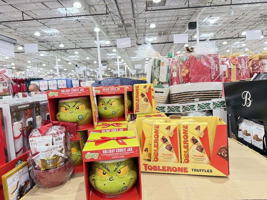 A decorative Grinch-themed ceramic cookie jar filled with praline cookies, featuring bright green holiday artwork.
