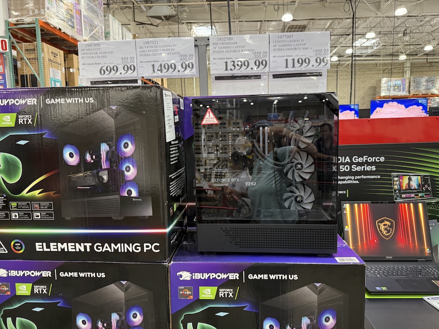 A glass-sided iBUYPOWER gaming desktop with internal RGB lighting sits on a display counter