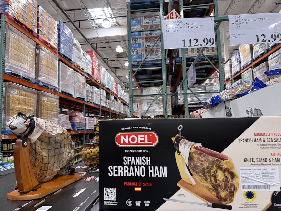 A full Serrano ham leg displayed in a long box, including a wooden stand and carving knife