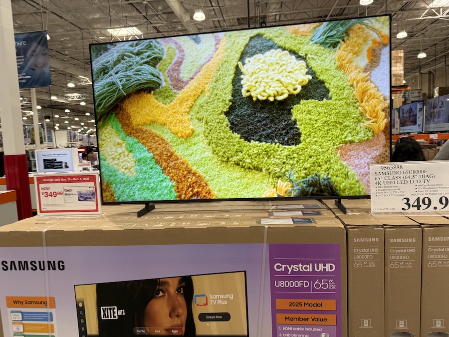 A Samsung 65-inch Crystal UHD 4K Smart TV is displayed on a shelf, showing bright demo visuals.