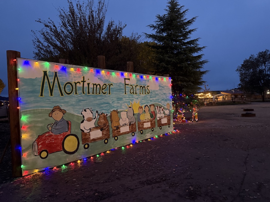 A large Mortimer Farms banner illuminated with holiday lights in the evening.