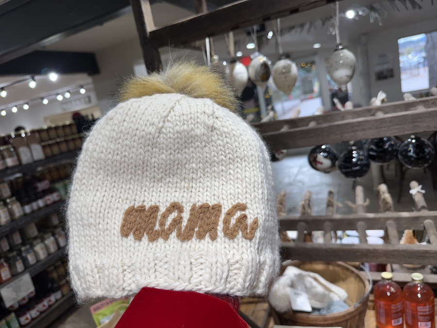 A cozy knitted winter hat embroidered with the word “mama,” displayed among seasonal apparel.