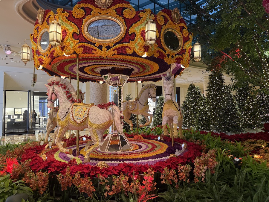 A vibrant floral carousel decorated for Christmas, made entirely of fresh flowers with festive accents and holiday lighting.