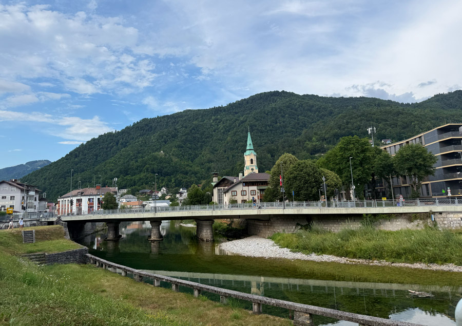 Bridge over the Idrijca River with a church spire and forested hills in Idrija, Slovenia