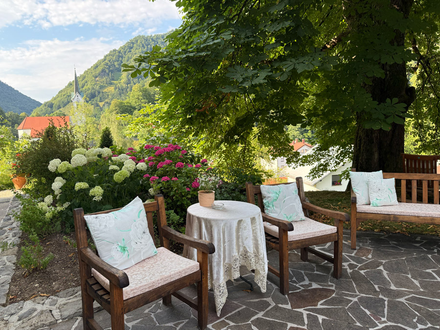 Garden seating at Kendov Dvorec overlooking a church and forested mountains