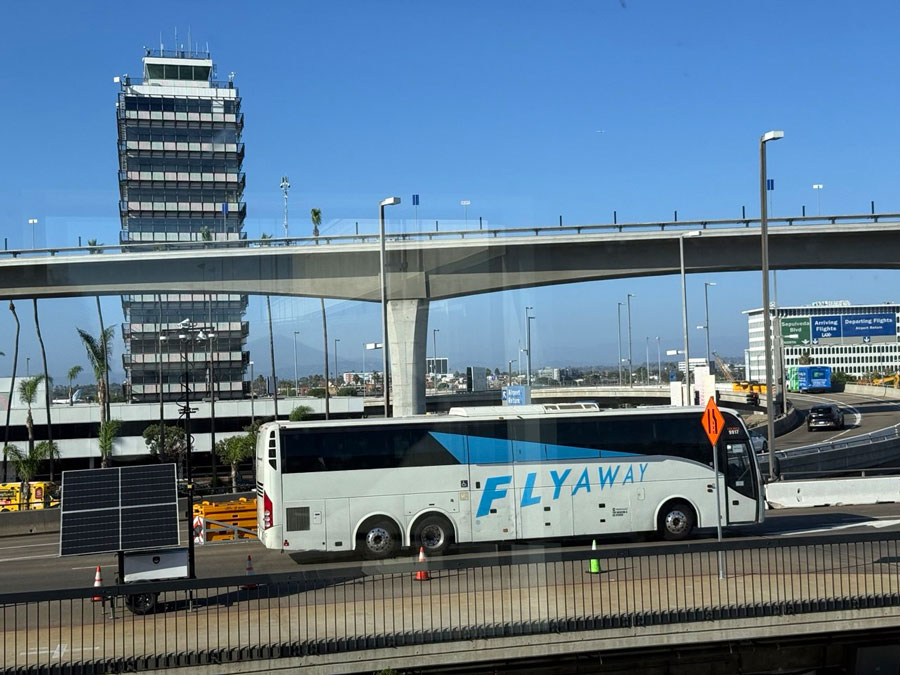 LAX FlyAway coach beside airport roadways, with the control tower in the background.